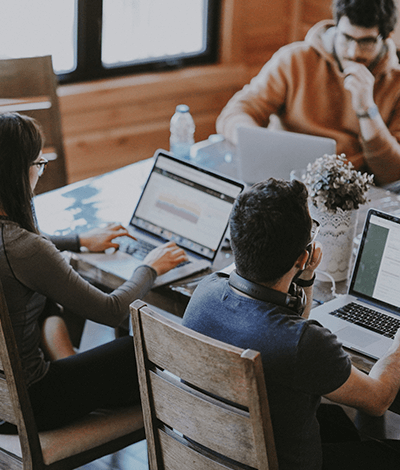 Three people sitting at a table together working on their laptops